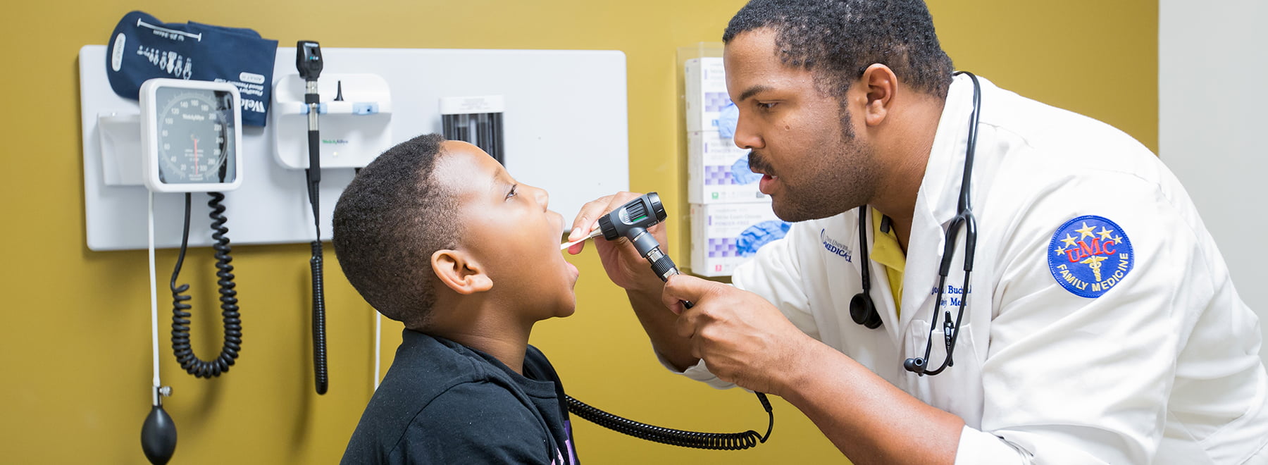 Doctor examining child's throat with scope and tongue depressor.